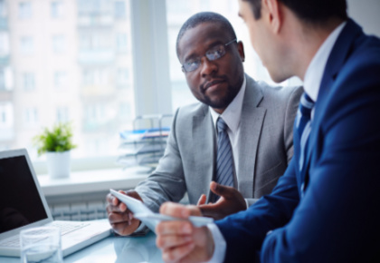 Two men talking at table next to laptop